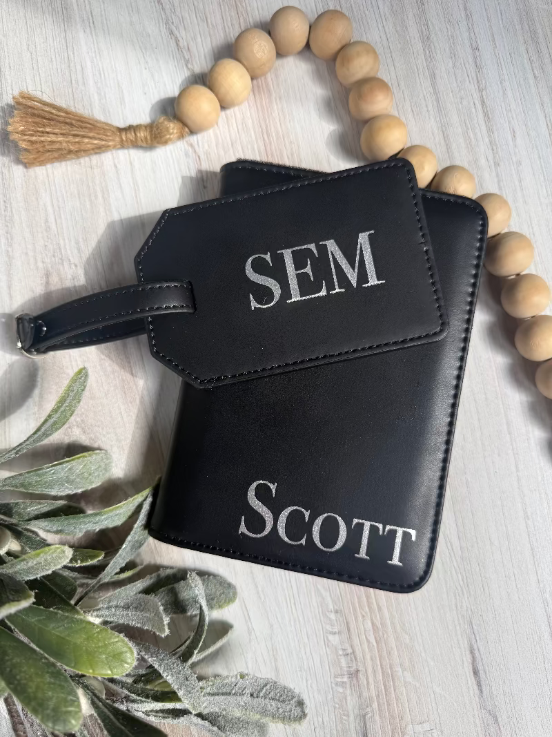 Two black leather luggage tags with 'SCOTT' and 'SEM' text on a light wooden surface with decorative elements.