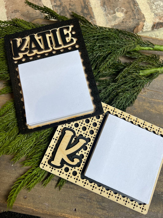 Decorative sticky note holder with 'Katie' and 'K' design on a wooden surface with greenery.