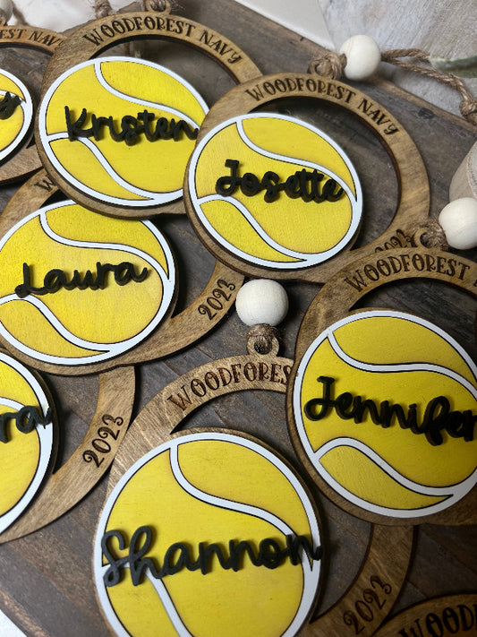 Wooden tennis ball-shaped ornaments with names engraved on a wooden surface.