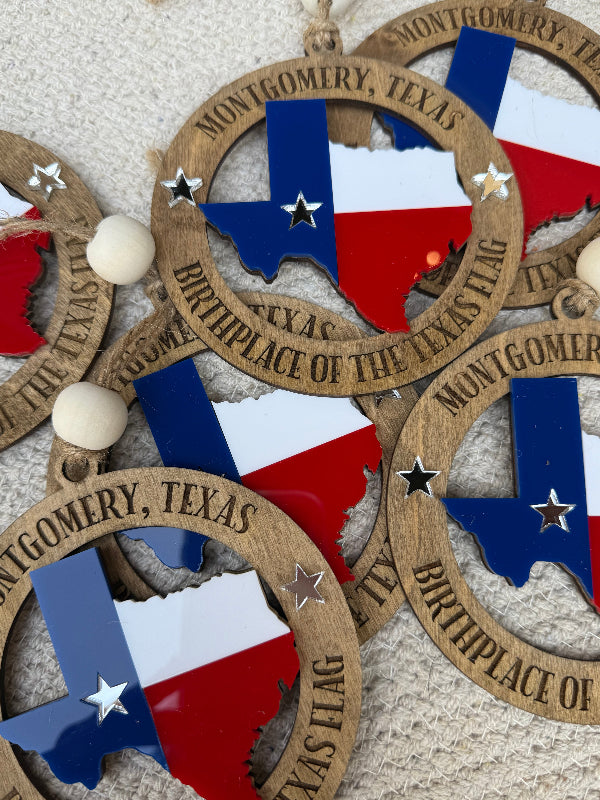 Wooden ornaments with Texas flag design and 'Montgomery, Texas' text on a textured surface.