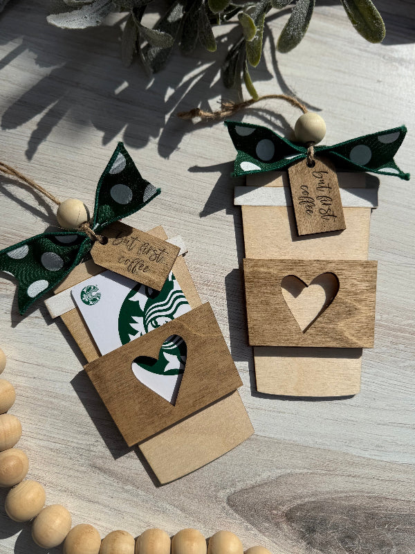 Wooden coffee cup ornaments with heart cutouts and a gift card on a wooden surface.