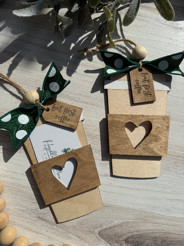 Wooden coffee cup-shaped gift tags with heart cutouts and green ribbons on a wooden surface.