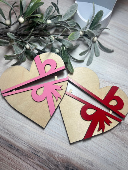 Two heart-shaped gift holders with pink and red bows on a wooden surface with mistletoe.