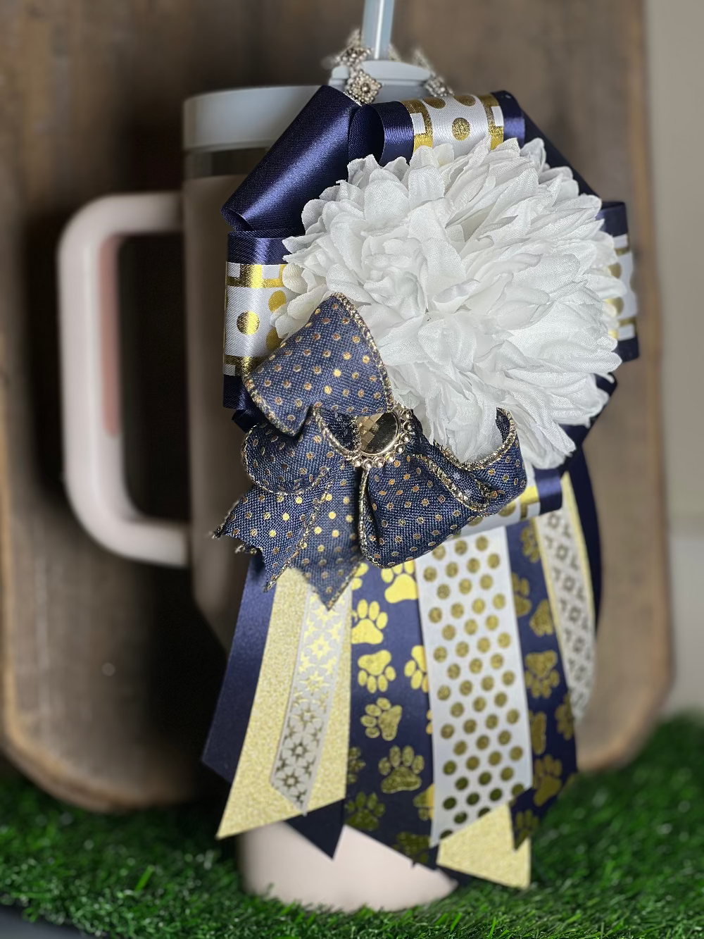 Decorative mug with a white flower and blue and gold ribbon against a neutral background