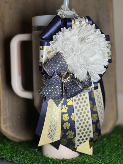 Decorative mug with a white flower and blue and gold ribbon against a neutral background
