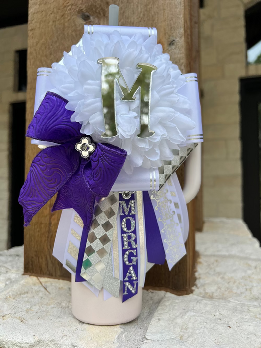 Decorative mini mum with a purple bow, white flowers, and a letter 'M' on a wooden surface.
