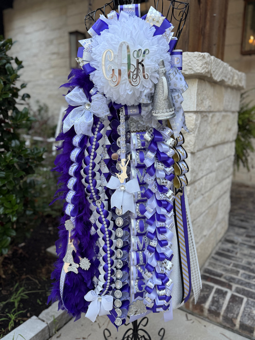Decorative mum with ribbons and monogram on a stand outdoors. Willis High School, custom braids.