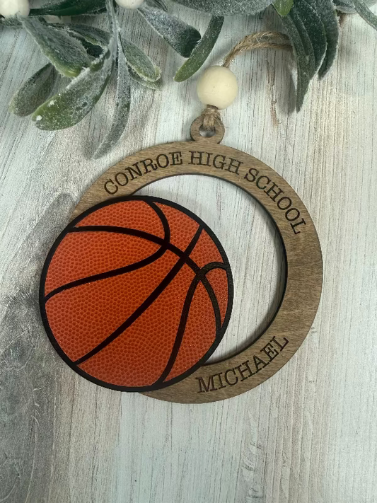 Basketball-themed ornament with 'Conroe High School' and 'Michael' engraved, on a wooden surface.