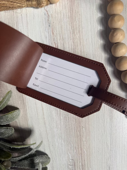 Brown leather luggage tag with white label on a light wooden surface