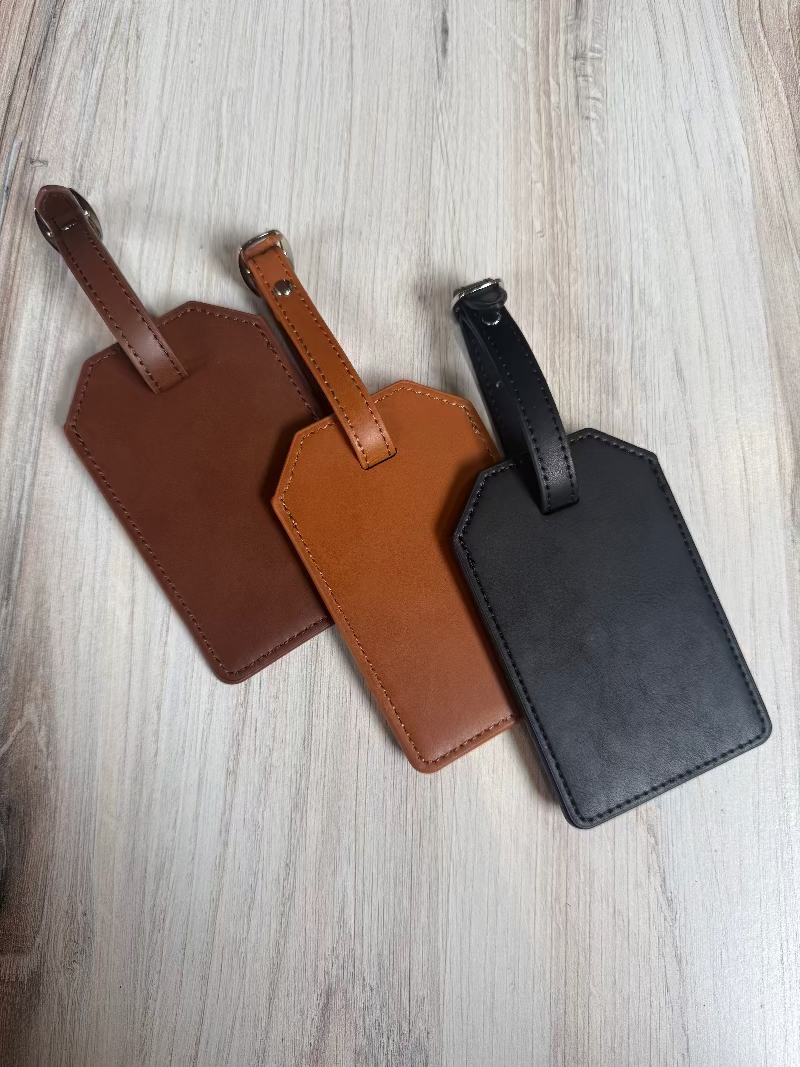 Three leather luggage tags in brown and black on a light wooden surface