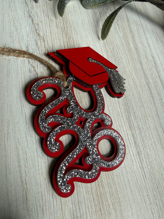 Decorative red and silver ornament with a graduation cap on a light wooden surface
