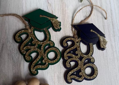 Graduation-themed ornaments with numbers '2026' and caps on a light wooden surface.