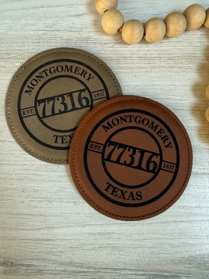 Two leather coasters with 'Montgomery 77316 Texas' engraving on a leatherette surface.