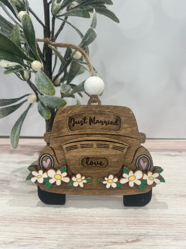 Wooden ornament shaped like a vintage car with 'Just Married' and 'Love' text, surrounded by flowers on a light surface.