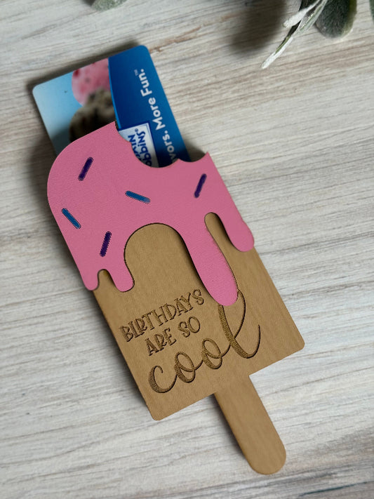 Ice cream popsicle-shaped laser-cut gift card holder with pink top and 'Birthdays are so cool' text on a wooden surface.