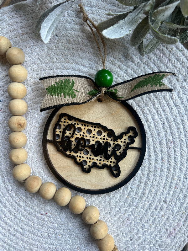 Wooden ornament with USA map design on a textured surface with beads and greenery.