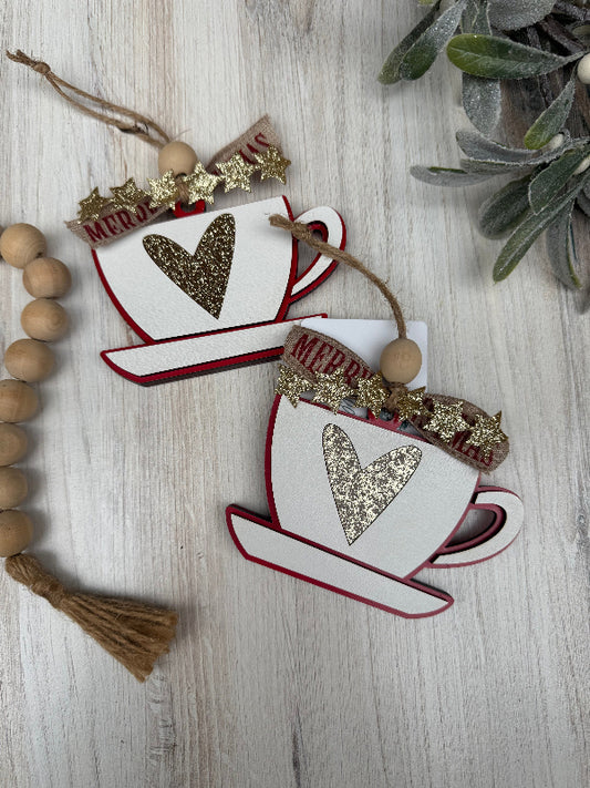 Decorative ornaments shaped like coffee cups with heart designs on a wooden surface.