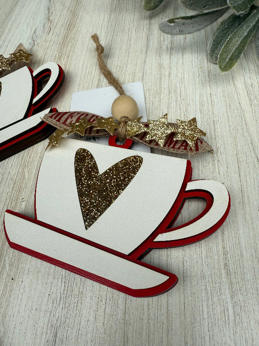 Decorative Christmas ornament shaped like a teacup with a heart, on a wooden surface.