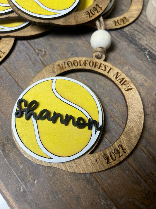 Wooden ornament with yellow tennis ball design and 'Shannon' text on a wooden surface.